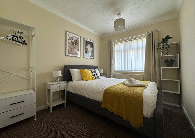 Bedroom with black bed, yellow throw, white nightstand, framed wall art, and shelving unit