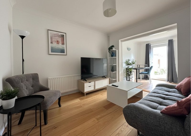 Bright living room with grey sofa, TV unit, wooden flooring and patio doors to garden