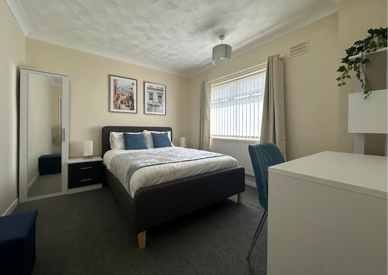 Bedroom with double bed, mirror, desk, window with blinds and potted plant