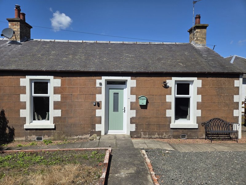 Red brick single-story cottage with white window frames, green door, and slate roof