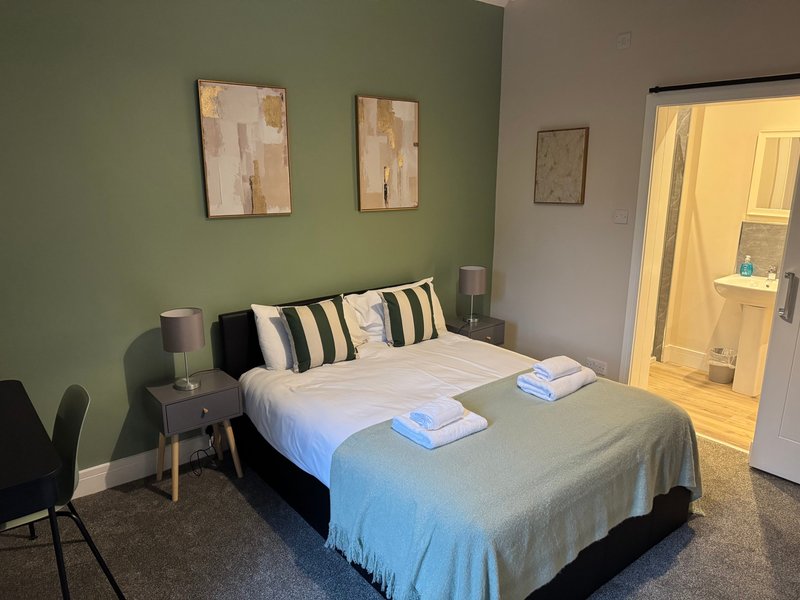 Bedroom with double bed, striped pillows, green accent wall, and ensuite bathroom visible