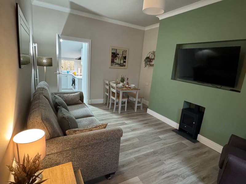 Open-plan living room with grey sofa, dining table, TV, and green accent wall