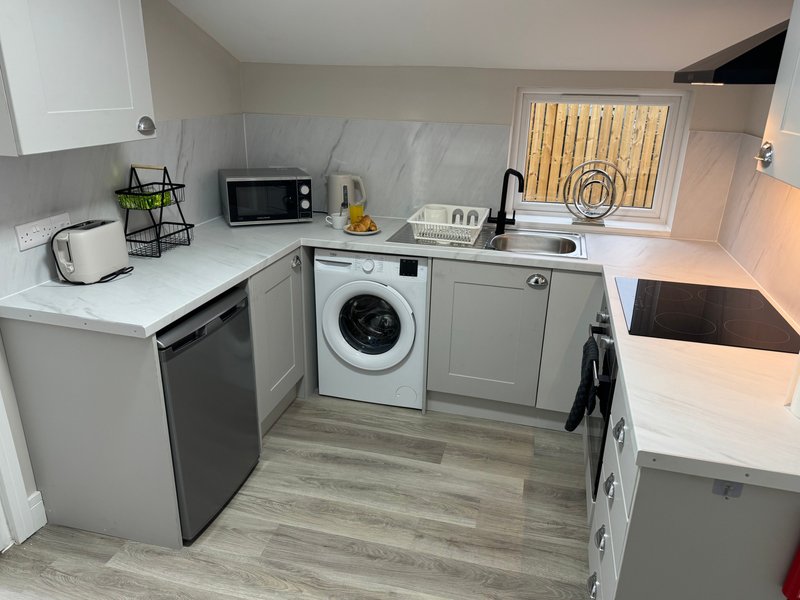 Modern kitchen with white countertops, gray cabinetry, washing machine, and stainless steel sink