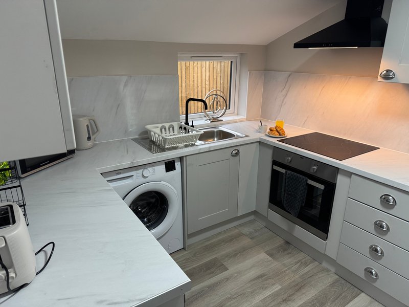 Modern kitchen with white cabinetry, marble countertop, integrated appliances and washing machine