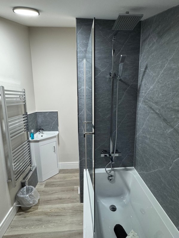 Modern bathroom with dark tile shower, white bathtub, vanity sink and heated towel rail