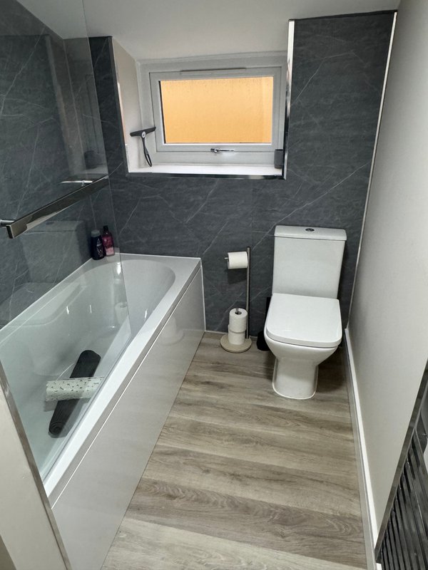 Modern bathroom with bathtub, toilet, dark tile walls and wooden floor