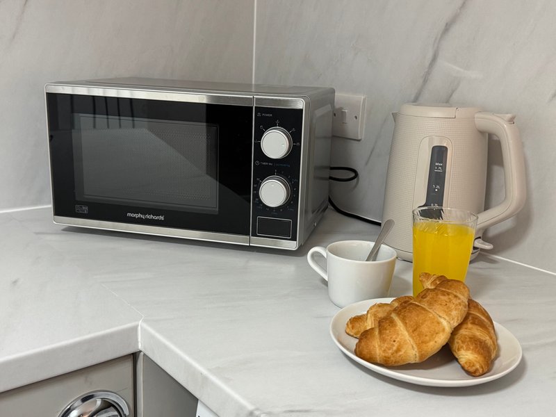 Kitchen counter with microwave, kettle, croissants on plate and orange juice