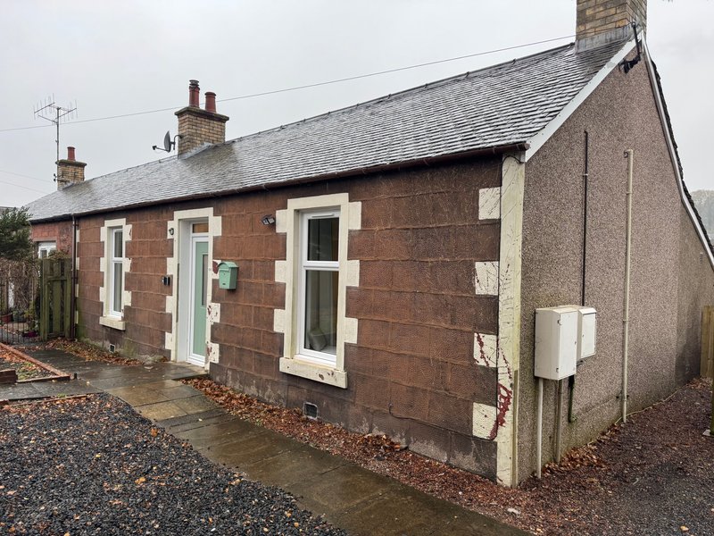 Brick cottage exterior with green and cream doors, gravel driveway and slate roof
