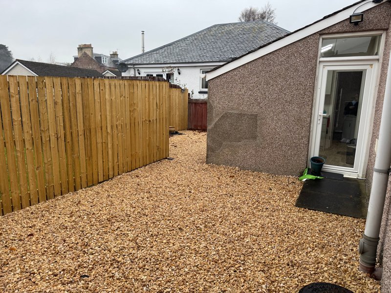 Exterior patio area with gravel surface, wooden fence, and access door to property