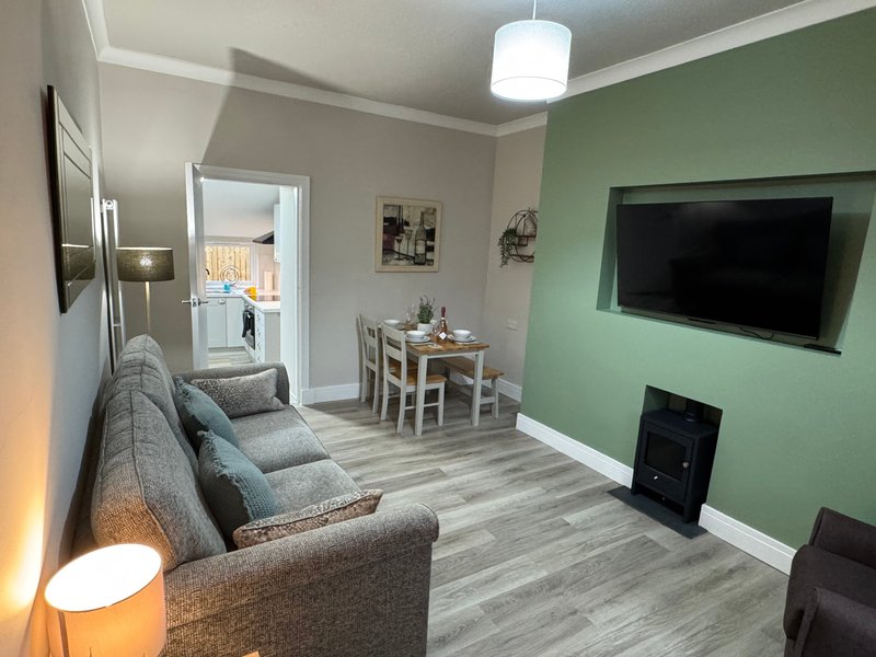 Open-plan living room with grey sofa, dining table, green accent wall and wall-mounted TV