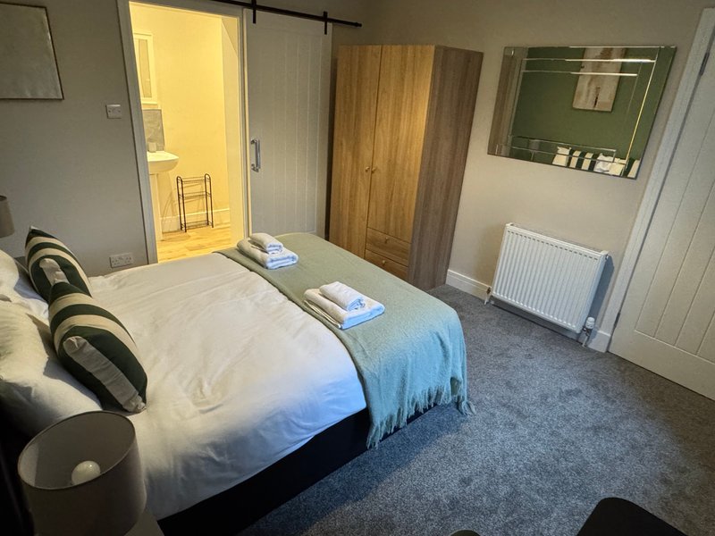 Bright bedroom with double bed, wooden wardrobe, radiator and ensuite bathroom visible