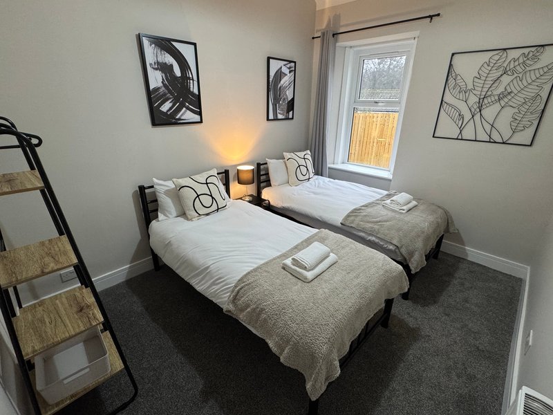 Twin bedroom with two single beds, neutral bedding, wall art, window with yellow blind and bedside lamp