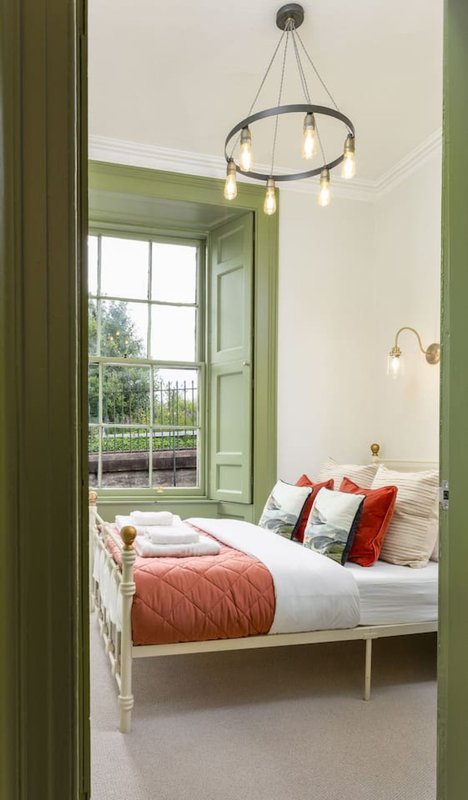 Bright bedroom with single bed, green-framed window, pendant light fixture and cushions