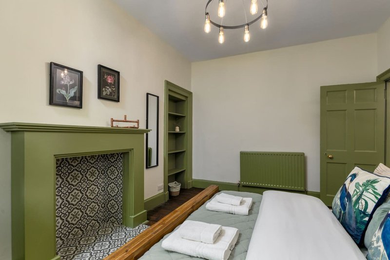 Bedroom with green fireplace, double bed, framed wall art, pendant lighting and shelving