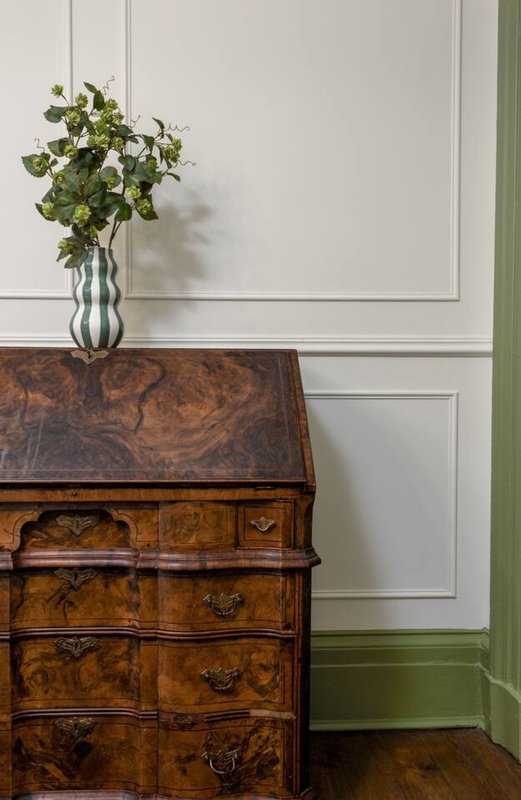 Antique wooden dresser with fresh flowers in glass vase against paneled wall