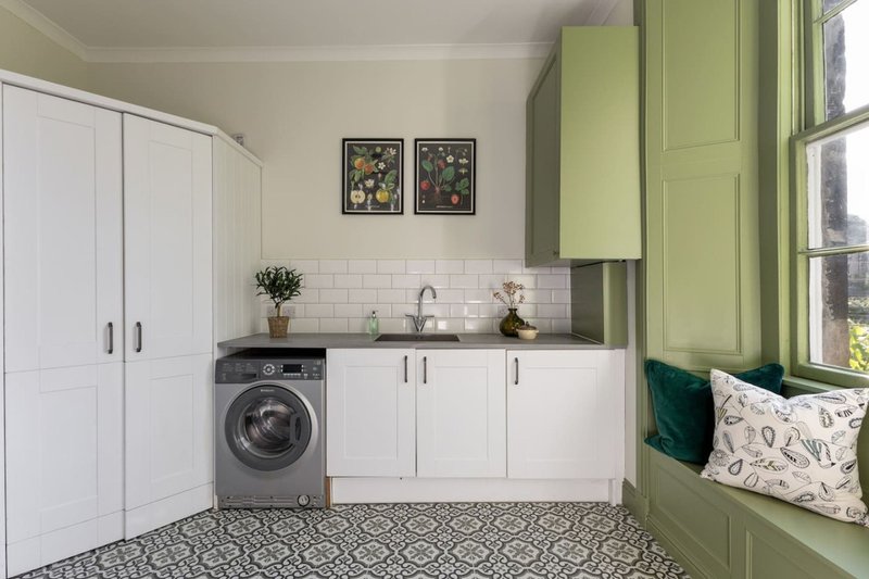 Modern laundry room with washing machine, white cabinetry, green accents and window seat