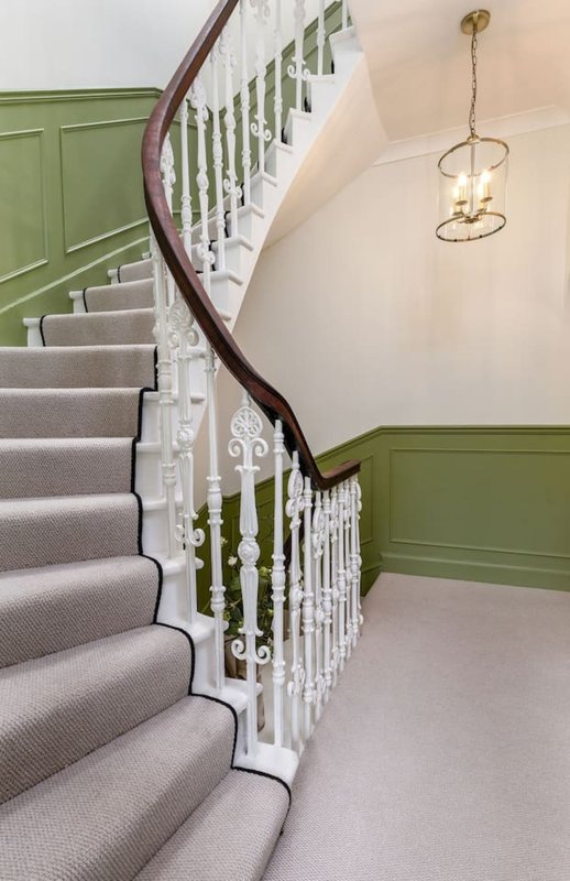 Staircase with curved dark wood handrail, white spindles, grey carpet runner, and green panelled walls