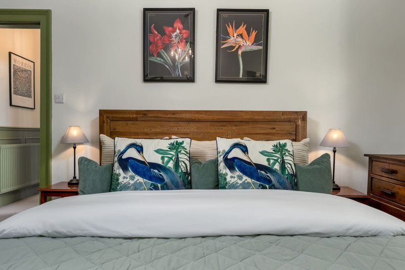 Bedroom with wooden bed frame, decorative pillows, white bedding, and framed flower artwork