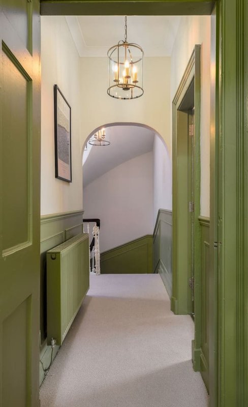 Hallway with green painted walls, pendant light fixture, and staircase entrance