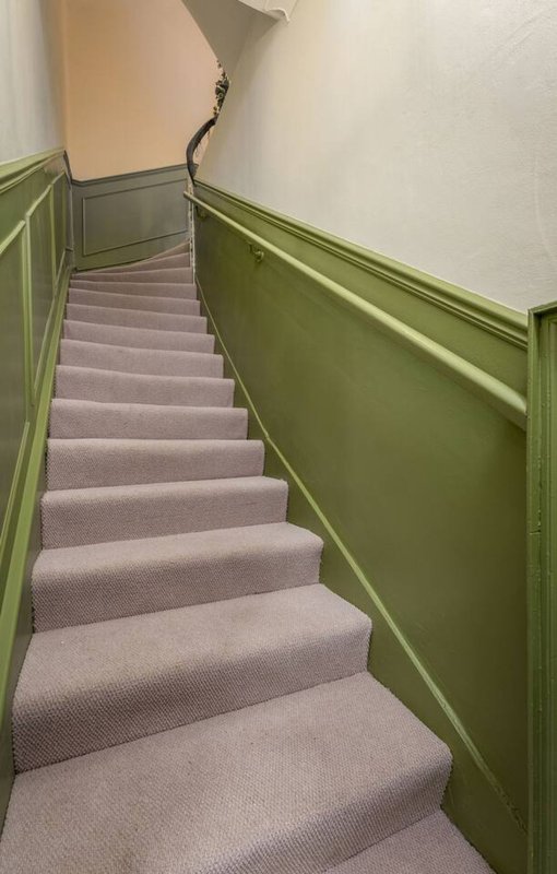 Staircase with grey carpet, green painted wall panelling and black metal handrail