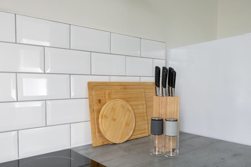 Kitchen counter with white subway tile backsplash, wooden cutting board, knife block, and glass containers