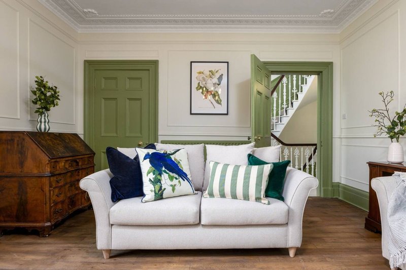 Bright living room with white sofa, green doors, wooden furniture and botanical artwork