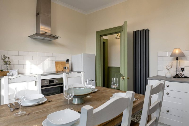 Open-plan kitchen and dining area with white cabinetry, wooden table, and green doorway