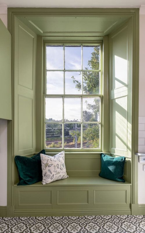 Green window seat with cushions overlooking countryside, multi-pane windows and scenic views