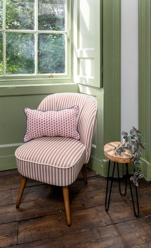 Pink striped armchair with cushion beside window, small side table with plant decoration