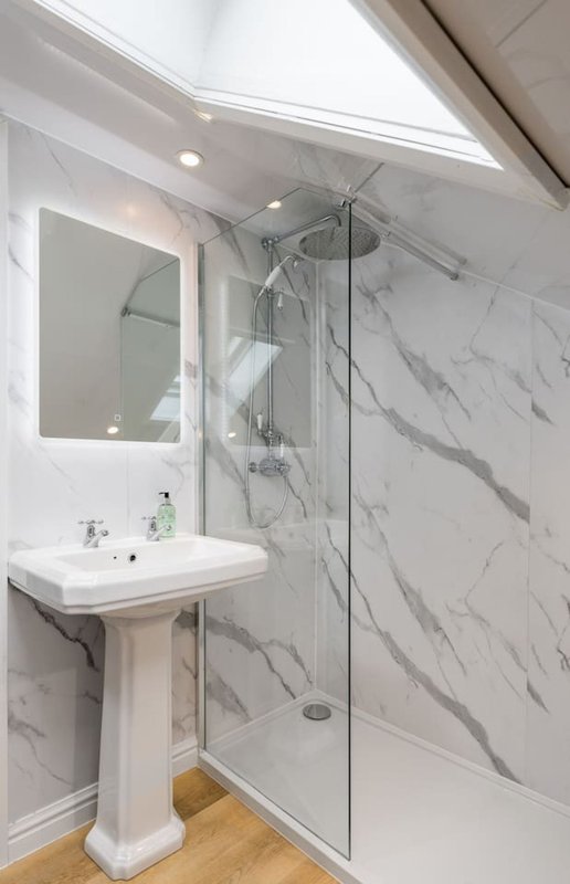 Modern bathroom with marble-effect tiles, pedestal sink, illuminated mirror and walk-in shower enclosure