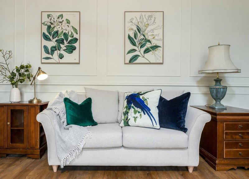 Bright living room with white sofa, green and navy cushions, wooden side tables and botanical wall art