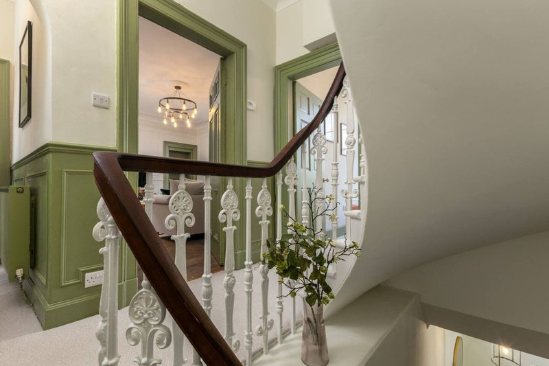 Hallway with green-framed doors, dark wooden staircase railing, and decorative spindles