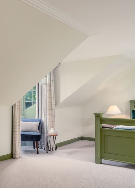 Bright attic bedroom with sloped ceiling, green wooden furniture, and window with curtains