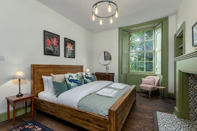 Bedroom with wooden bed, green window frame, framed wall art, and pink armchair