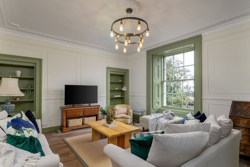 Bright living room with gray sofas, wooden coffee table, TV, green shelving and pendant light fixture