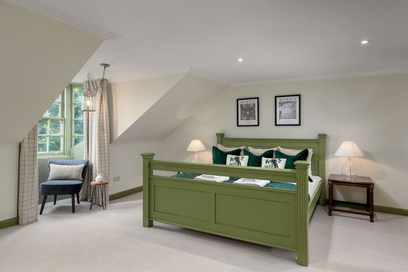 Bright attic bedroom with green wooden bed, armchair, large window and framed wall art