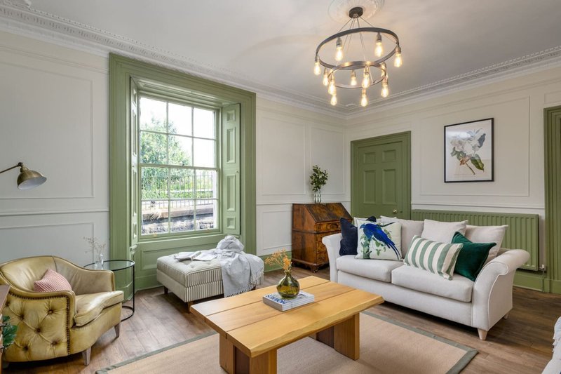 Bright living room with green-trimmed windows, cream sofa, wooden coffee table, and pendant lighting