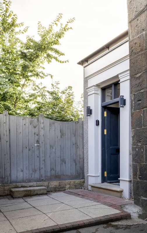 Modern entrance with dark blue door, white frame, grey fence, and paved patio area