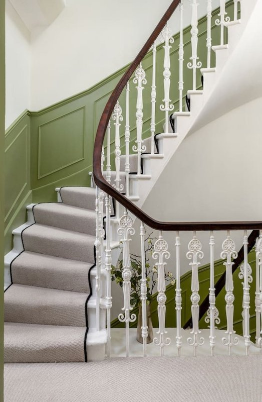 Interior staircase with green panelled wall, grey carpet runner, white ornamental balusters and dark wood handrail