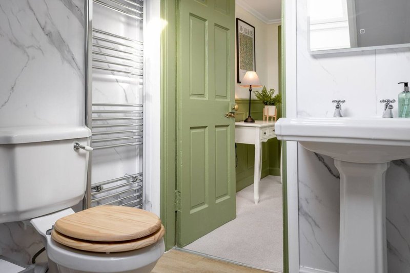 Modern bathroom with toilet, pedestal sink, green door, marble tiles and heated towel rail