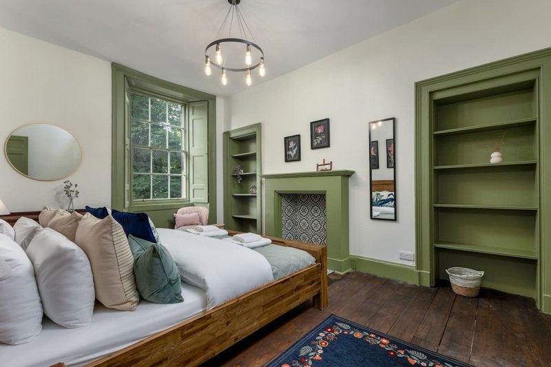 Bedroom with wooden bed, white bedding, green built-in shelving, and pendant ceiling light