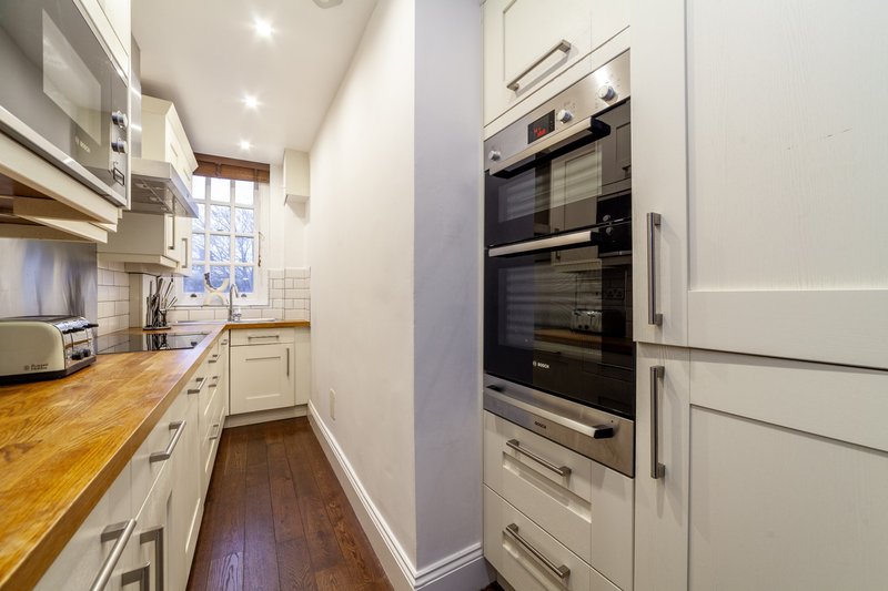 Modern galley kitchen with cream cabinetry, wooden countertop, stainless steel appliances and window