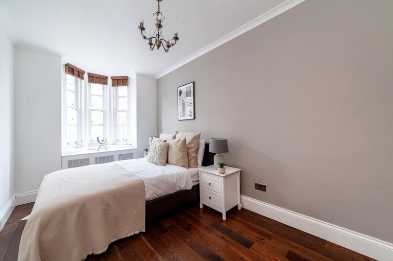Bedroom with double bed, white nightstand, bay windows and chandelier