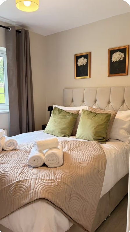 Bedroom with upholstered headboard, patterned bedding, green cushions and rolled towels