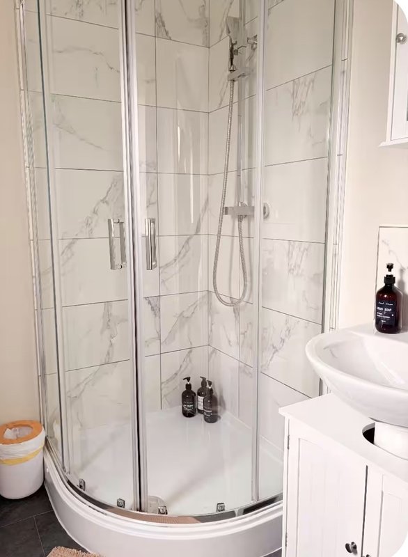 Modern bathroom with corner shower enclosure, marble-effect tiles, white sink and storage cabinet