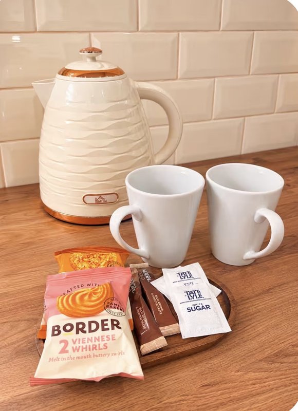 Kitchen counter with cream kettle, two white mugs, packaged biscuits and tea sachets