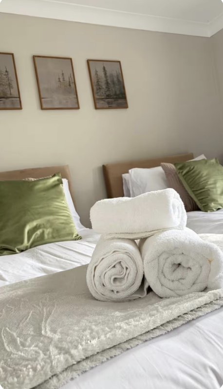 Bedroom with double bed, rolled white towels, green cushions, and framed wall art