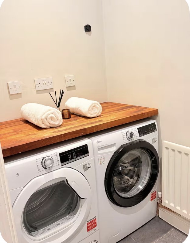 Laundry room with two front-load washing machines and wooden countertop with rolled towels