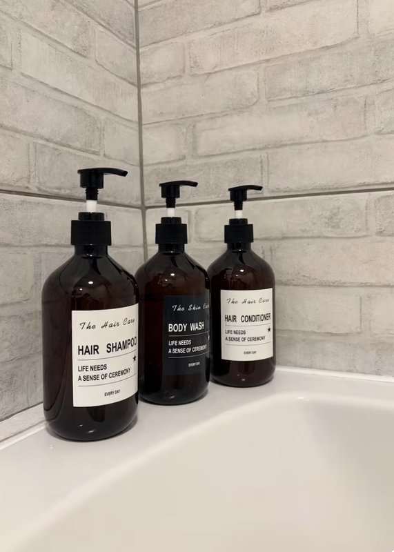 Bathroom shelf with three pump bottles of toiletries against white brick wall