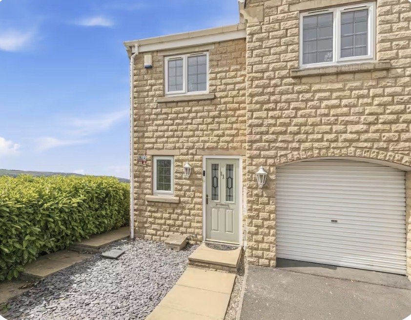 Stone-built house exterior with garage, gravel drive, hedge and clear sky